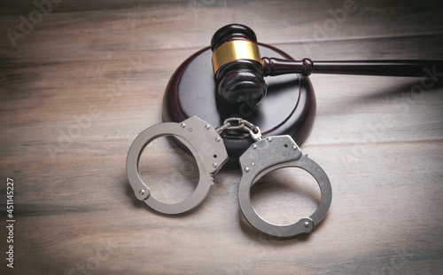 Metal handcuffs and judge gavel on the wooden background.