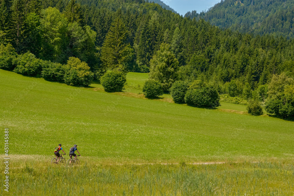 sporty mountain bikers in a green, idyllic alpine landscape sporty mountain bikers in a green, idyllic alpine landscape