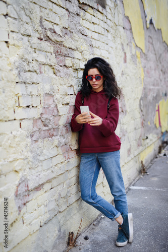 Portrait of young woman standing outdoors on street in city, using smartphone.