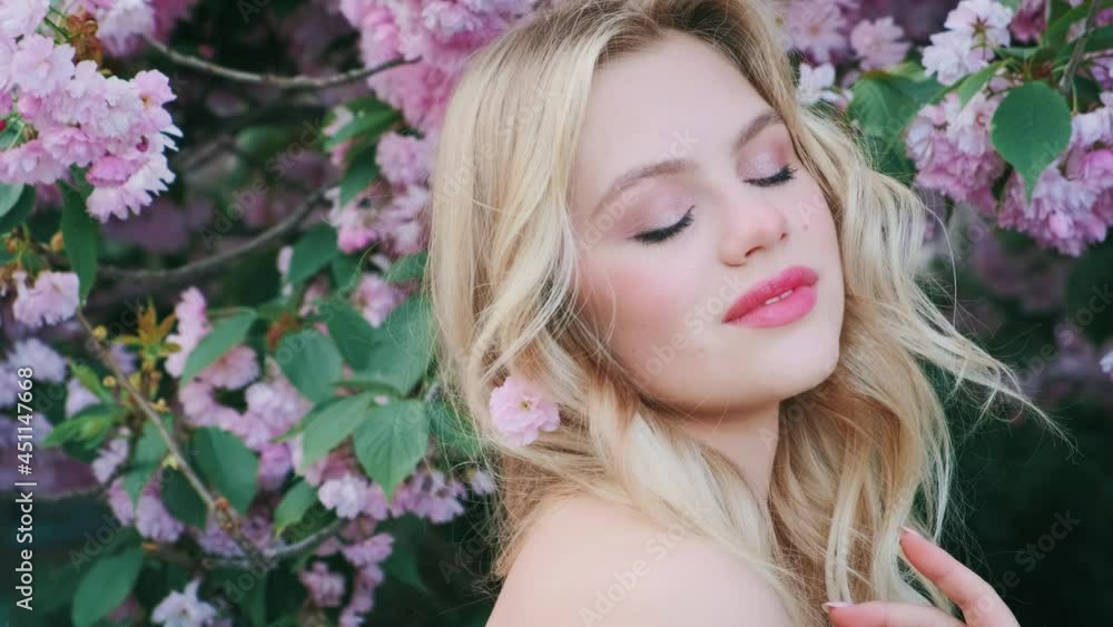 Close up portrait fairy fantasy happy woman. Fashion model girl poses look at camera. Green leaves sakura tree pink flowers. pink lips blush eye shadow. Beauty smiling face, blue eyes long blond hair Close up portrait fairy fantasy happy woman. Fashion model girl poses look at camera. Green leaves sakura tree pink flowers. pink lips blush eye shadow. Beauty smiling face, blue eyes long blond hair