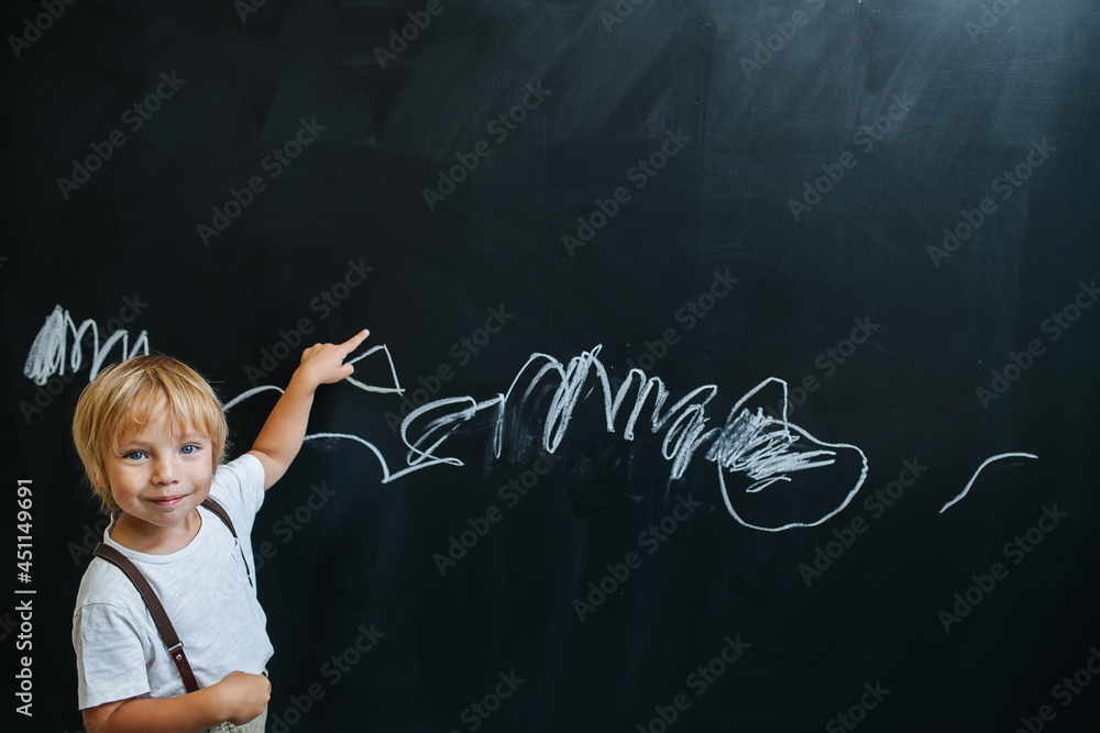 Handsome playful little boy writing on a board, pretending to be a teacher