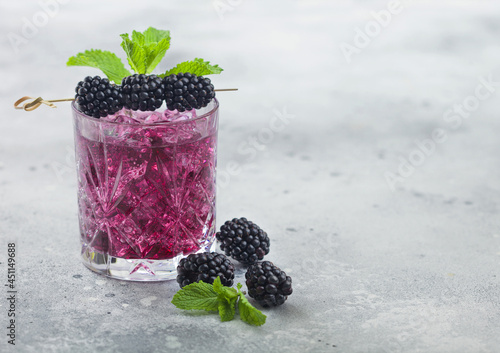 Glass of refreshing summer cocktail with blackberry, ice and mint on light background. Soda and alcohol mix.
