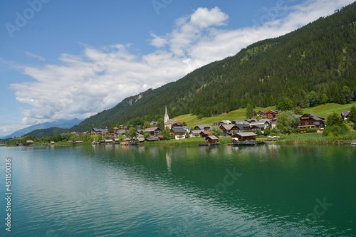 Panorana view of the village "Techendorf" with blue sky and the lake "Weissensee" in the foreground, taken in summer