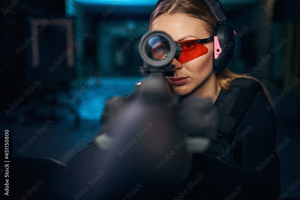 Serious woman using a telescopic sight mounted on the weapon - obrazy, fototapety, plakaty 