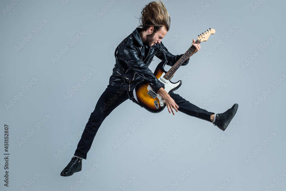 emotional bearded rock musician playing electric guitar in leather jacket and jumping, guitar player - obrazy, fototapety, plakaty 