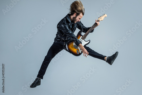 emotional bearded rock musician playing electric guitar in leather jacket and jumping, guitar player photo