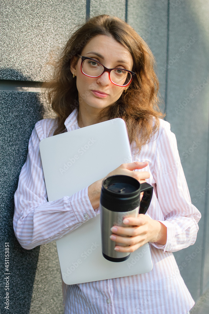 Female portrait of young woman with silver laptop and cup of coffee waiting for a meeting near dark grey wall in the morning, remote job, coffeebreak, smart student concept Female portrait of young woman with silver laptop and cup of coffee waiting for a meeting near dark grey wall in the morning, remote job, coffeebreak, smart student concept
