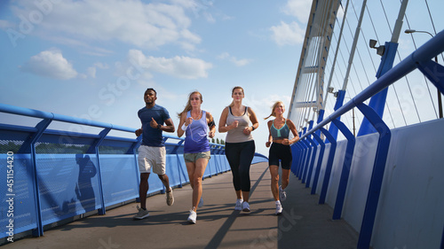 Group of young and old people running outdoors on bridge in city.