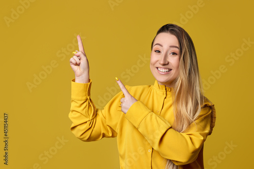 young woman pointing away on yellow background