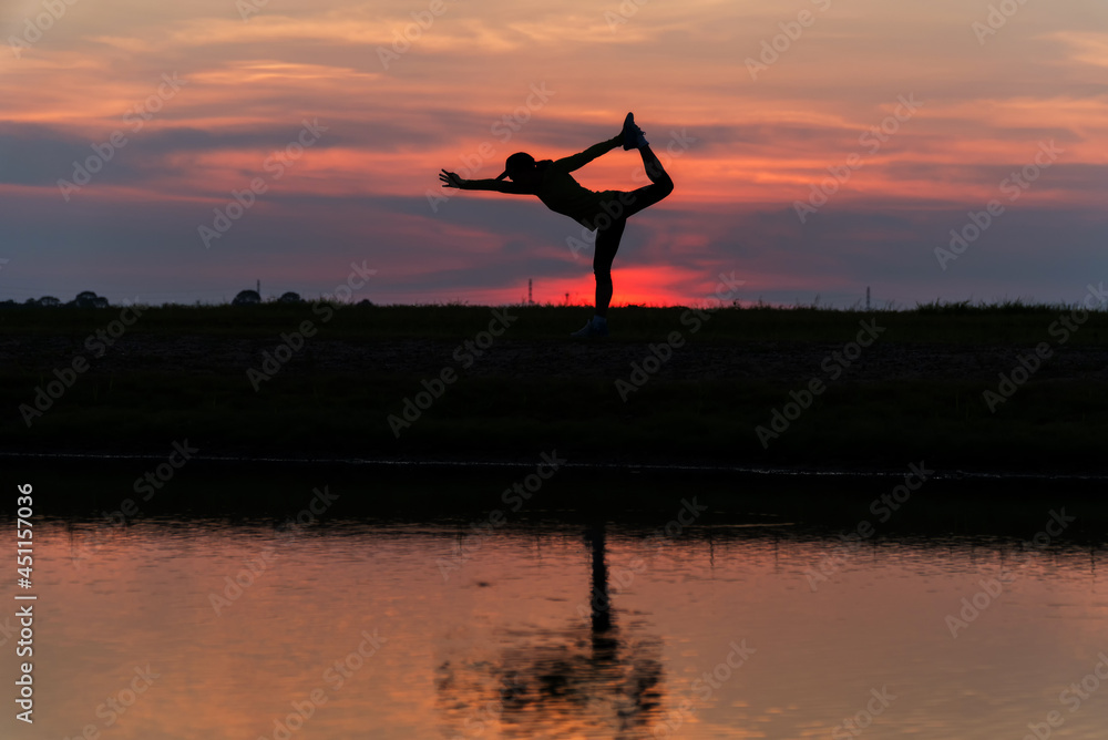 woman practicing yoga during surrealistic sunset at the seaside. healthy concept and workout. Silhouette asian woman exercise yoga pose at twilight sunset time with reflection on river.