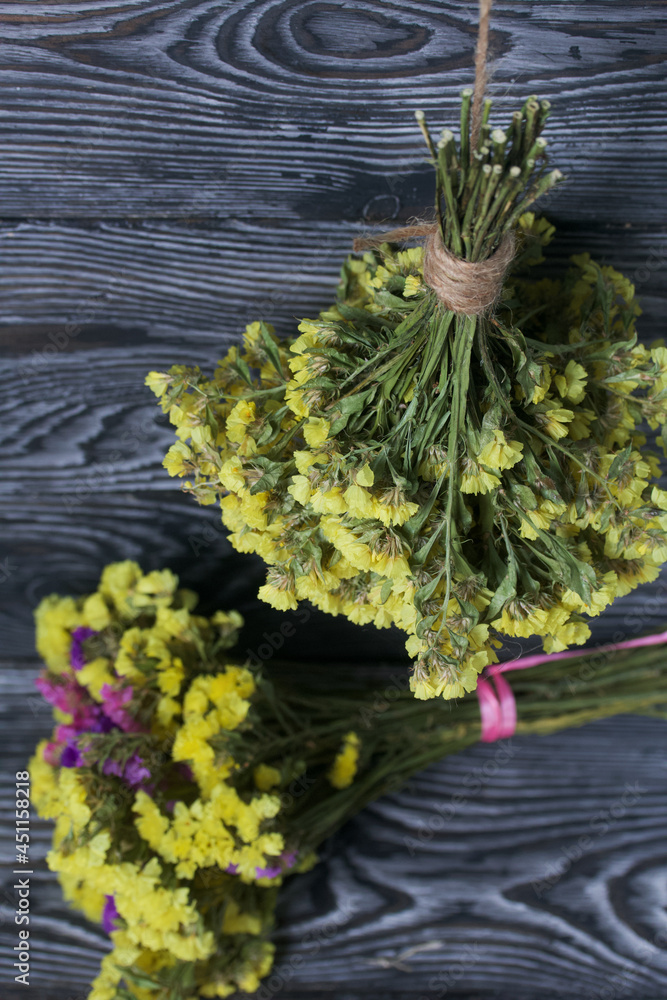 Two bouquets of statice. One is yellow, the other is multi-colored. Against the background of pine boards.