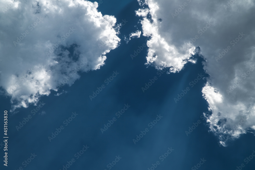 Dark blue sky with white and gray clouds passing the sun's rays