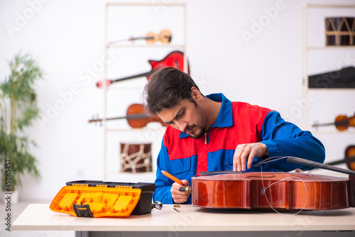 Fotografie Young male repairman repairing musical instruments at workplace
