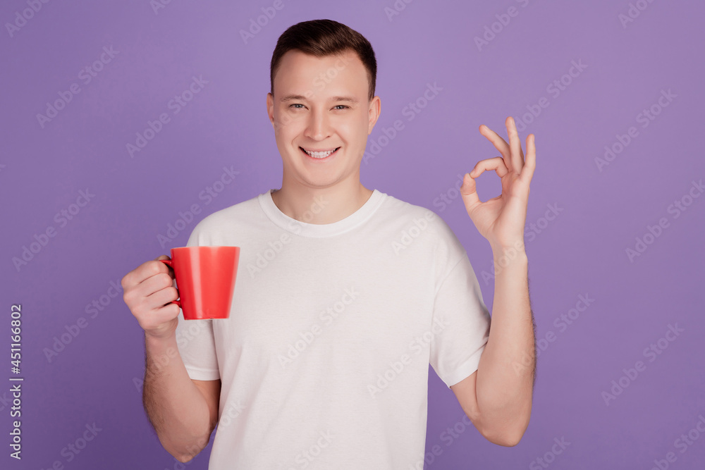 Portrait of handsome man hold cellphone coffee cup show okey gesture on purple background Portrait of handsome man hold cellphone coffee cup show okey gesture on purple background