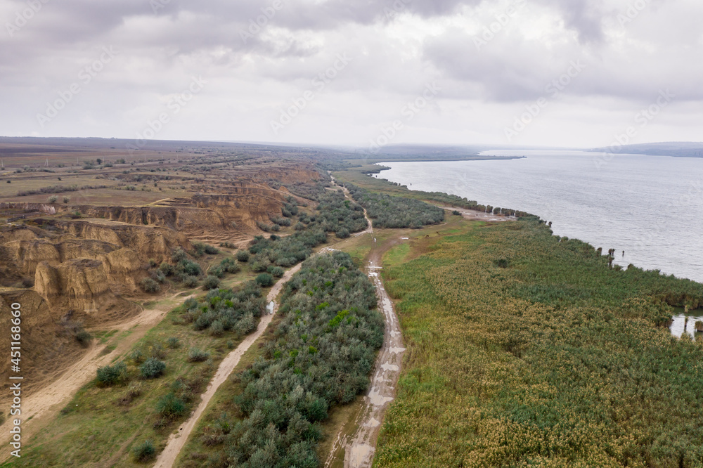Aerial view of a path along huge lake with beautiful sand dunes and green shore