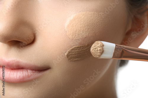 Obraz na płótnie Girl applying foundation and concealer with brush on white background, closeup