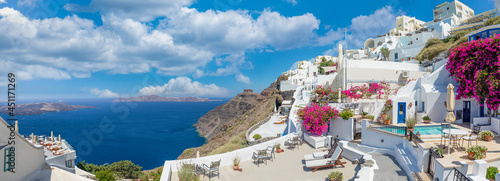 Sunny in Oia caldera panorama on Santorini island, Greece. Famous travel summer vacation destination. Flowers, white blue architecture, sunlight peaceful summer vibe. Inspirational panoramic landscape