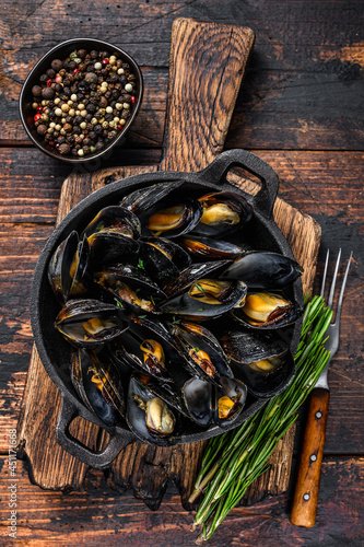 Mussels cooked with white wine sauce in a pan with herbs. Dark wooden background. Top view