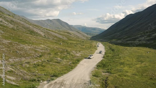 SUVs are driving on a dirt road in the valley of the Khibiny Mountains. Aerial view