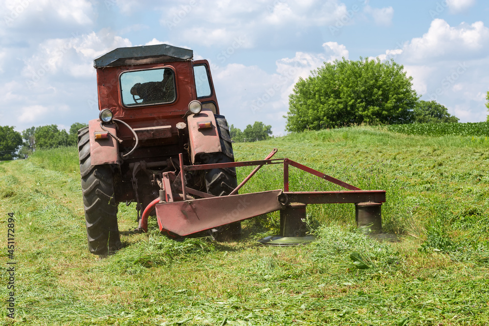 Obraz premium Rotary mower on small old tractor during operation on hayfield