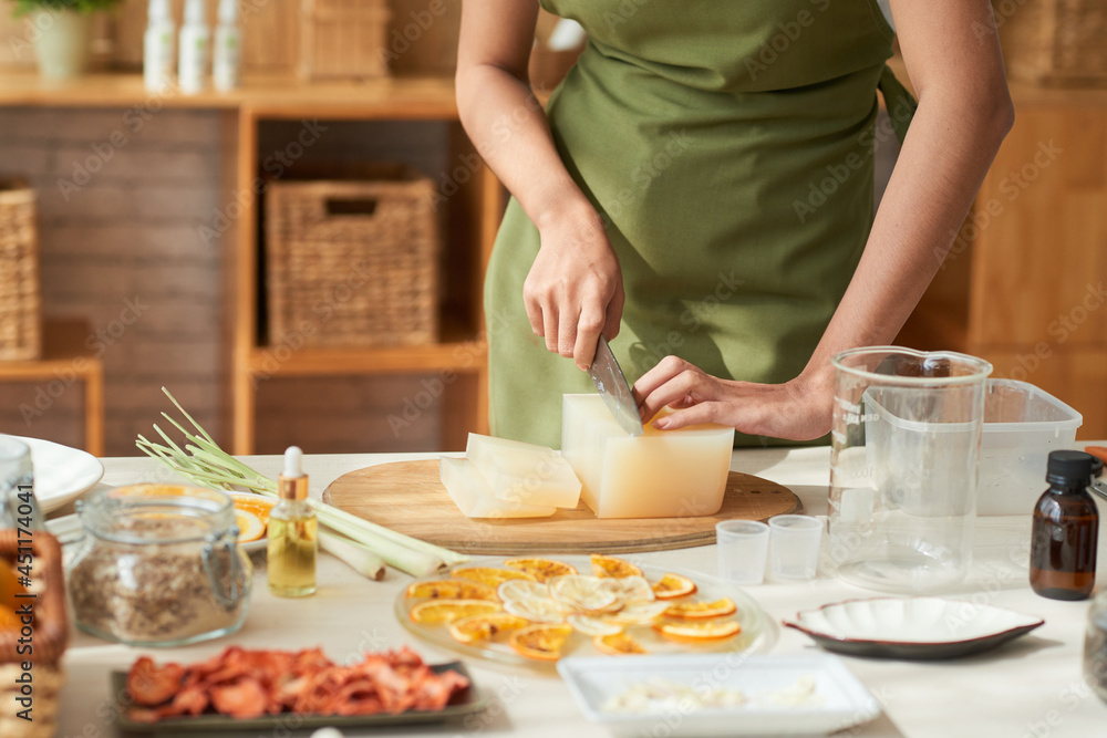 Hands of young woman in apron cutting soap base when making cleansing bars at home Hands of young woman in apron cutting soap base when making cleansing bars at home