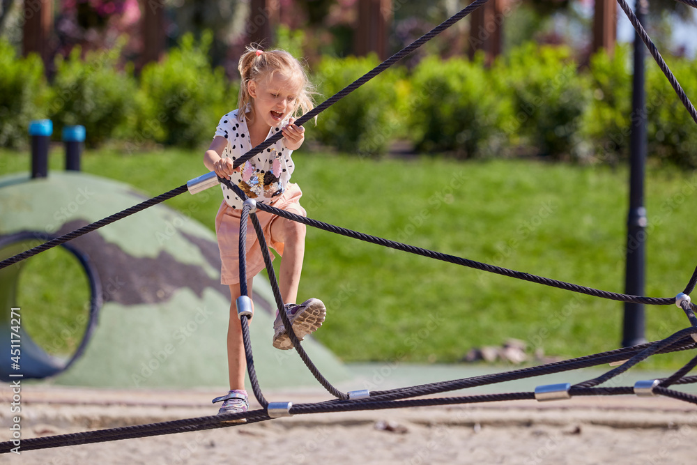 Active blonde girl is happy to climb the ropes in playground in summer time Active blonde girl is happy to climb the ropes in playground in summer time