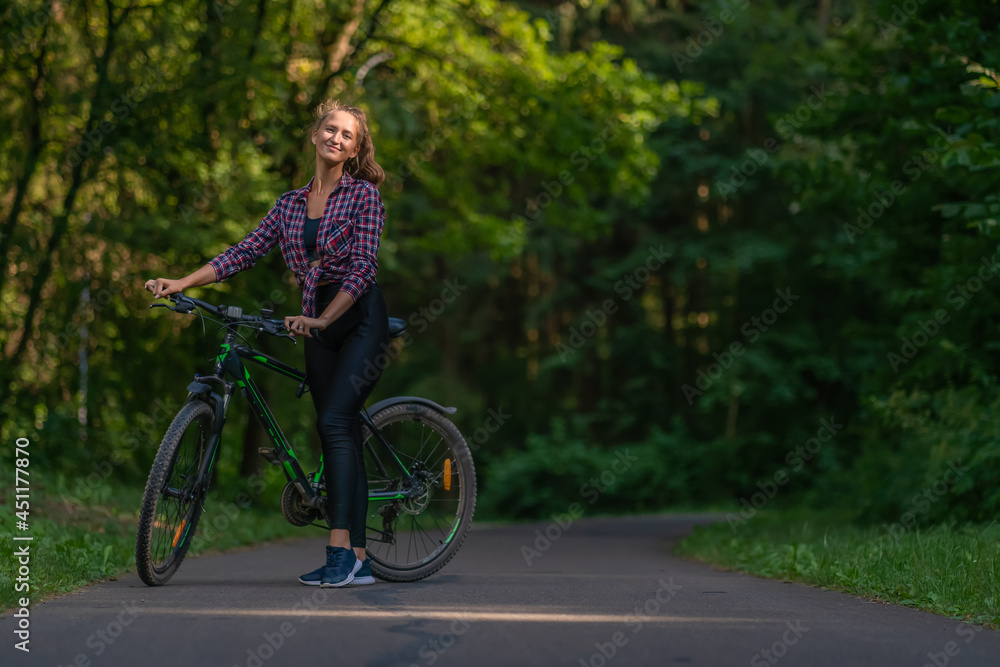 Young woman on a bicycle stands on the road in the park and looks at the camera, copy space Young woman on a bicycle stands on the road in the park and looks at the camera, copy space
