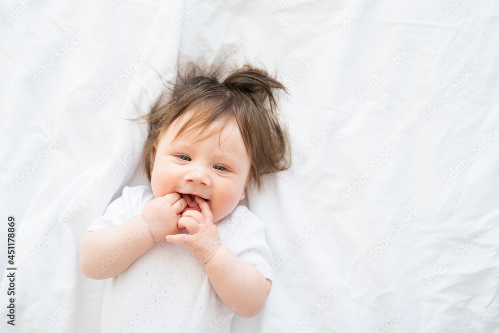 portrait of funny baby girl with finger in a mouth smiling and lying on a white bedding at home. portrait of funny baby girl with finger in a mouth smiling and lying on a white bedding at home.