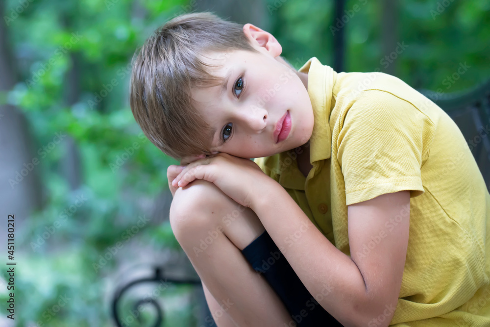 The sad little boy put his head on his knee. The child is bored. The sad little boy put his head on his knee. The child is bored.