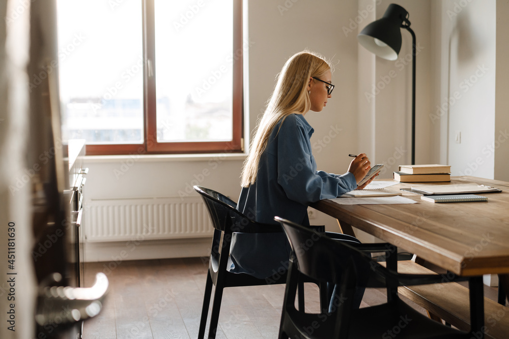 White blonde woman using mobile phone while working at home White blonde woman using mobile phone while working at home
