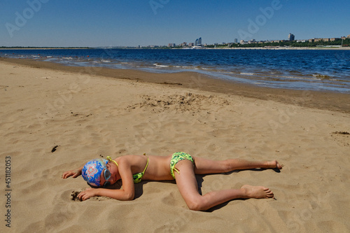 Summer sandy beach. The girl sunbathes sprinkled with sand. Children's summer vacation.