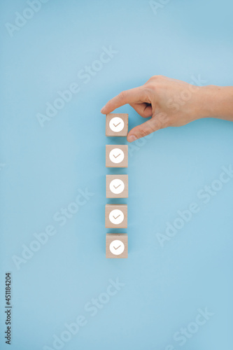 Female hand putting down the white tick marking wooden cube for checklist or to do list concept photo