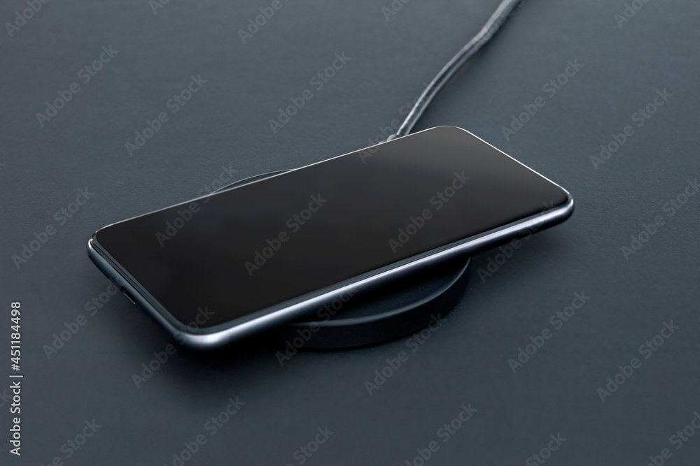 Close-up of luxury smartphone while recharging battery using wireless charger. Matt grey desk surface in background. Close-up of luxury smartphone while recharging battery using wireless charger. Matt grey desk surface in background.