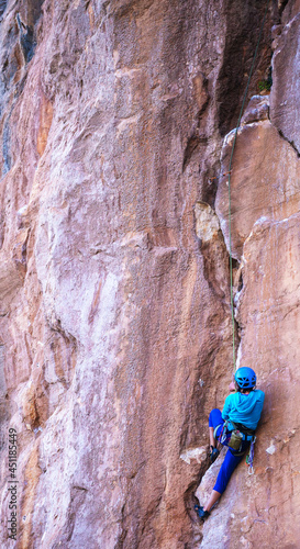 A woman in a helmet climbs a beautiful blue rock.