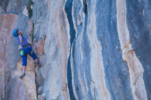 A woman in a helmet climbs a beautiful blue rock.