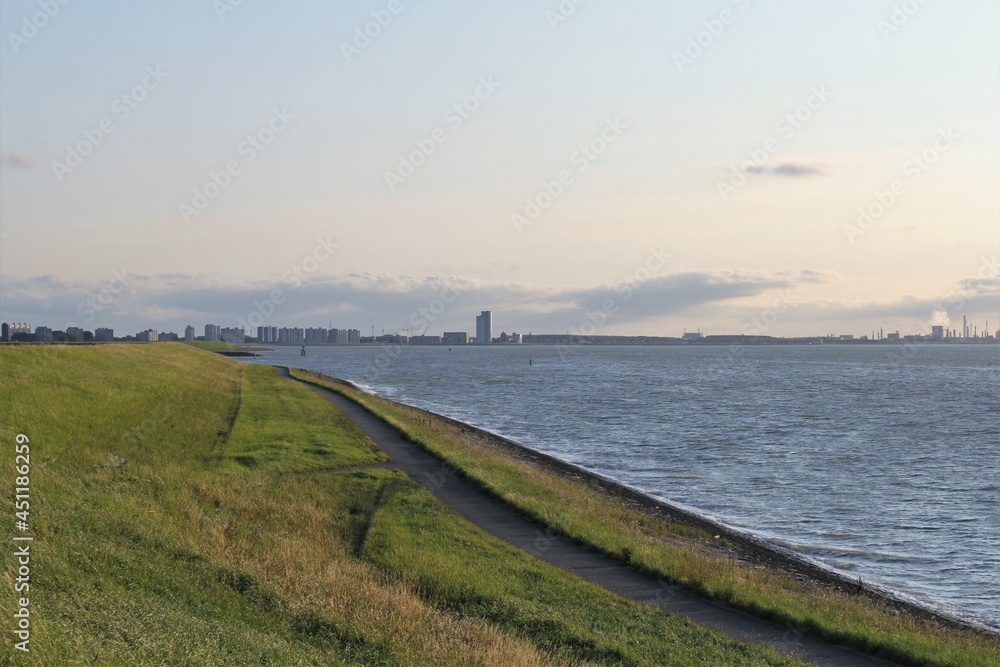 beautiful sea landscape at the dutch coast in zeeland with the skyline of Terneuzen in the background and the seawall with a road of the westerschelde sea in front