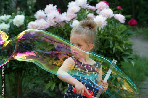 Girl playing with soap bubbles on a background of flowers