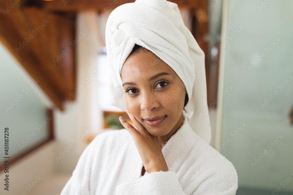 Portrait of smiling mixed race woman in bathroom touching face after moisturising, looking at camera Portrait of smiling mixed race woman in bathroom touching face after moisturising, looking at camera