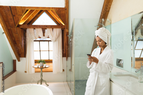 Mixed race woman in bathroom using smartphone and brushing her teeth photo