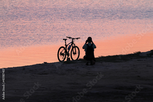 Man beside the bike takes a picture of the sunset near the water