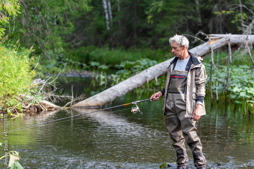 Portrait of fisherman in waders with spinning rod on the river. Spinning fishing photo