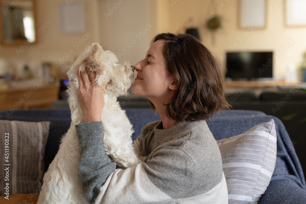 Smiling caucasian woman in living room sitting on sofa embracing her pet dog Smiling caucasian woman in living room sitting on sofa embracing her pet dog