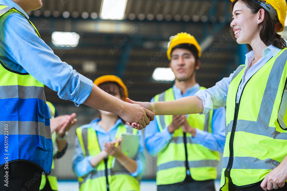 Factory employee of engineers, foreman, technicians and staff. Wear a mask, hard hat, and vest. shake hands to make a deal or celebrate success in the organization or warehouse. Teamwork concept. Factory employee of engineers, foreman, technicians and staff. Wear a mask, hard hat, and vest. shake hands to make a deal or celebrate success in the organization or warehouse. Teamwork concept.