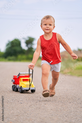 Cute Little Boy Plays in Outside with Toy Car. Boy Pulling Toy Car Behind Him