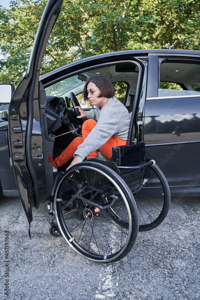 Woman in a wheelchair getting on the car at the drivers sit and preparing to the road Woman in a wheelchair getting on the car at the drivers sit and preparing to the road