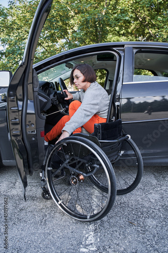 Woman in a wheelchair getting on the car at the drivers sit and preparing to the road