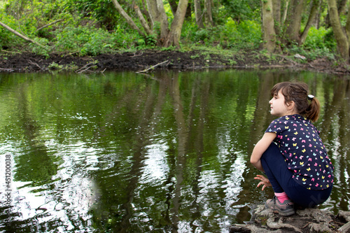 Fototapeta Naklejka Na Ścianę i Meble -  Girl sitting on the roots of a tree on the bank of a river