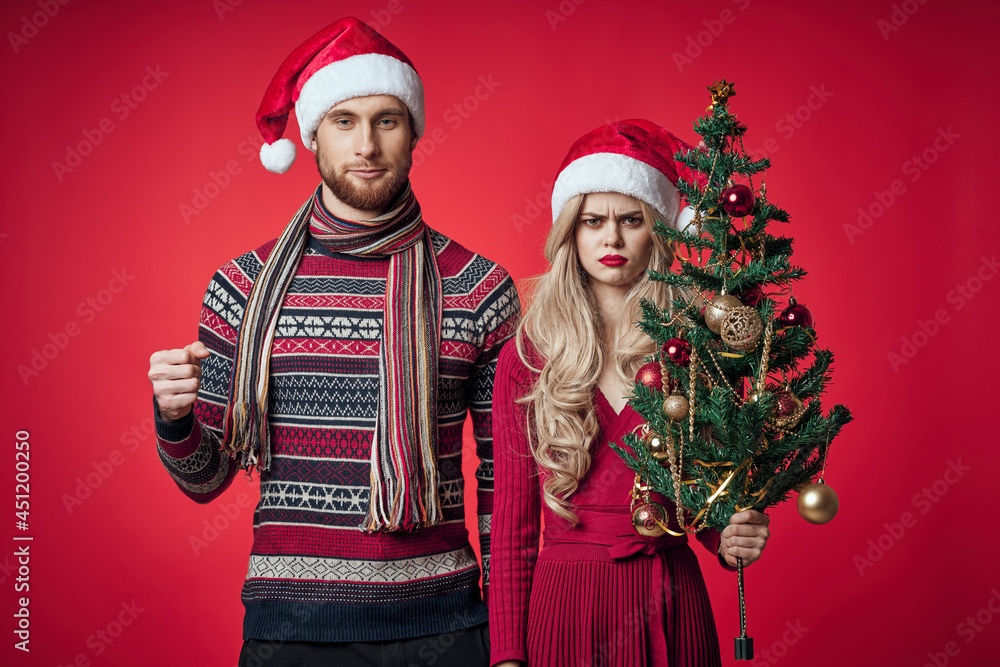 Fototapeta premium man and woman standing next to christmas tree toys lifestyle red background