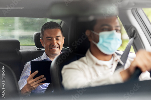 transportation, health and people concept - happy smiling male passenger with tablet pc computer and indian taxi driver wearing face protective mask for protection from virus disease driving car © Syda Productions