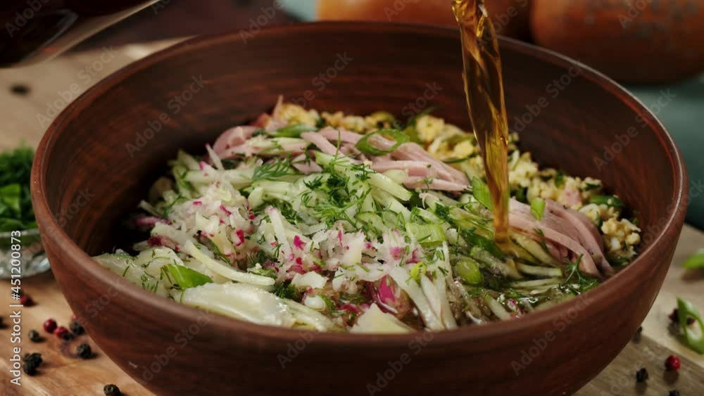 Pouring kvass into salad close-up, cooking okroshka, summer cold soup. Traditional Russian Cuisine. Ukrainian food in wooden bowl. Fresh homemade dish. Pouring kvass into salad close-up, cooking okroshka, summer cold soup. Traditional Russian Cuisine. Ukrainian food in wooden bowl. Fresh homemade dish.